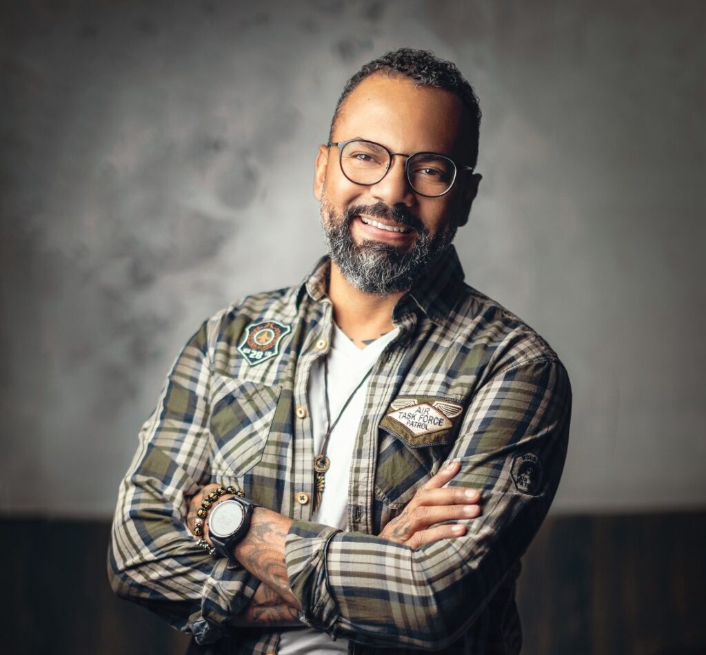 Alex de Carvalho smiling, wearing glasses and a checked shirt
